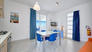 Une cuisine moderne équipée d’une cuisinière à gaz, d’un coin repas avec des chaises bleues, d’un téléviseur fixé au mur et d’un extincteur.