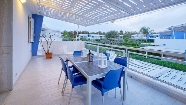 Un espace extérieur abrité, aménagé pour les repas, avec une table et des chaises, un pot de fleurs et une vue sur les bâtiments environnants.