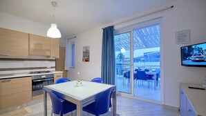Une cuisine moderne avec un coin repas, un téléviseur et une vue sur l’extérieur.