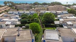 Il s’agit d’un quartier résidentiel composé de plusieurs immeubles à deux étages, chacun ayant un toit plat et des antennes paraboliques. On aperçoit des espaces verts et des arbres au premier plan, et une étendue d’eau en arrière-plan.