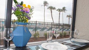 Ein Tisch für zwei, gedeckt mit einer blauen Vase voller Blumen, einem Glas Wasser und Blick auf einen Pool und Palmen.