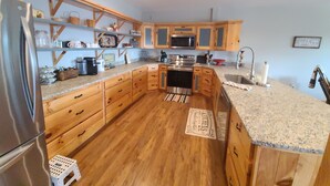 A spacious kitchen with wooden cabinets, a stainless steel refrigerator, granite countertops, and a central island with a sink.