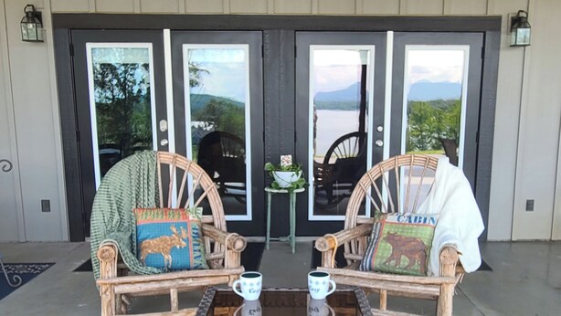 Two wicker chairs with cushions, a small table with two cups, and a view of a lake through a set of doors.