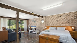 A modern bedroom with a brick wall, a wooden bed, a TV, and a desk.