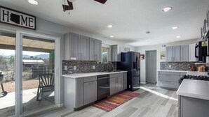 A modern kitchen with grey cabinets, a black refrigerator, and a tiled backsplash.