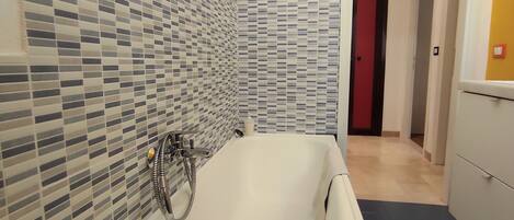Un baño moderno con una bañera independiente, paredes de azulejos y suelo de madera.