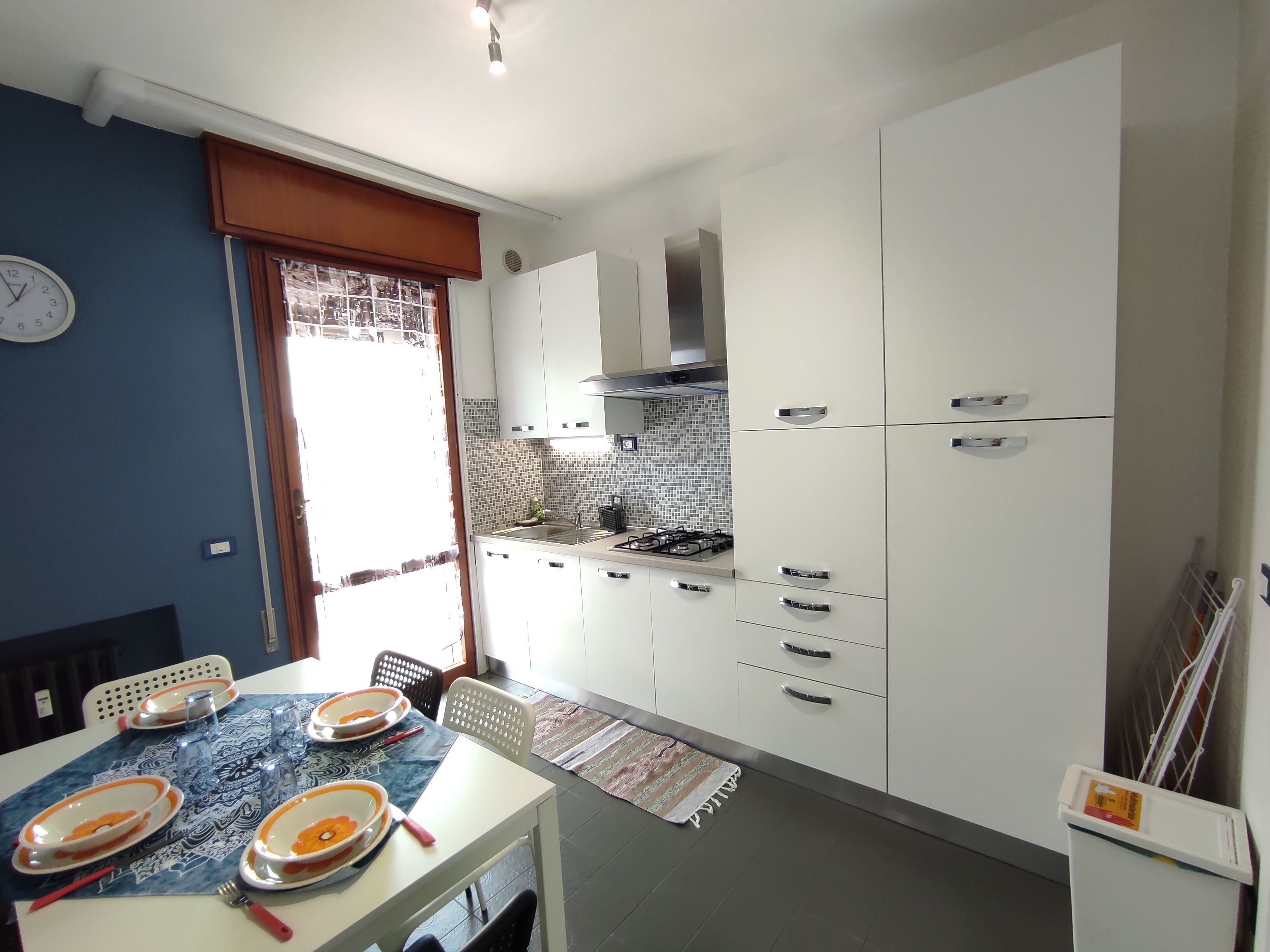 Une cuisine compacte avec des meubles blancs, une cuisinière à gaz et une table à manger pour quatre personnes.