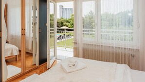 Ett hotellrum med en säng, ett badrum och en balkong med utsikt över grönområden och byggnader.