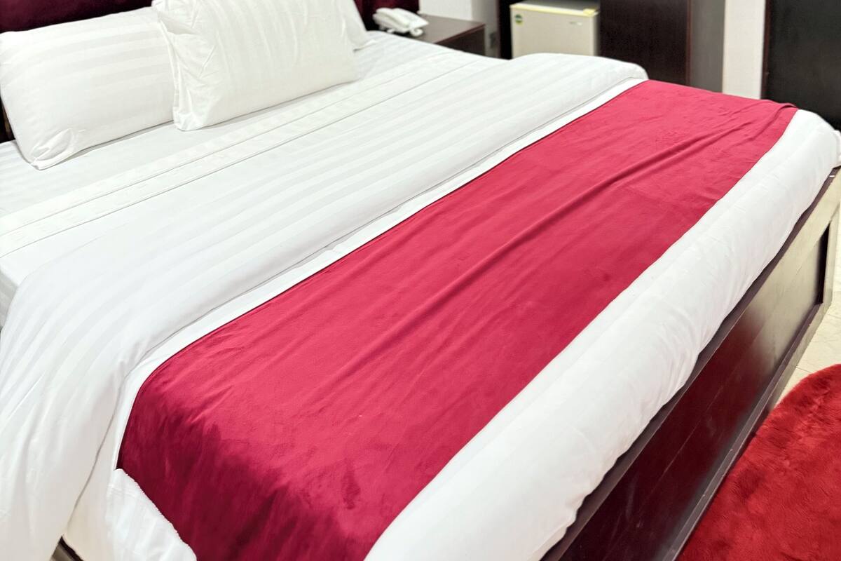 Un lit bien fait, recouvert d’une couvre-lit rouge et blanche, avec une tête de lit sombre et deux œuvres d’art encadrées accrochées au mur.