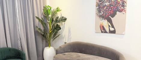 A modern living room with a grey sofa, green armchairs, a marble coffee table, a large potted plant, and a wall art piece.