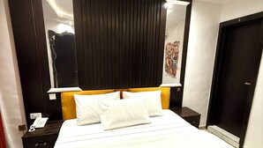 Una habitación de hotel con una cama grande, una mesita de noche con un teléfono, un armario oscuro y un espejo en la pared.