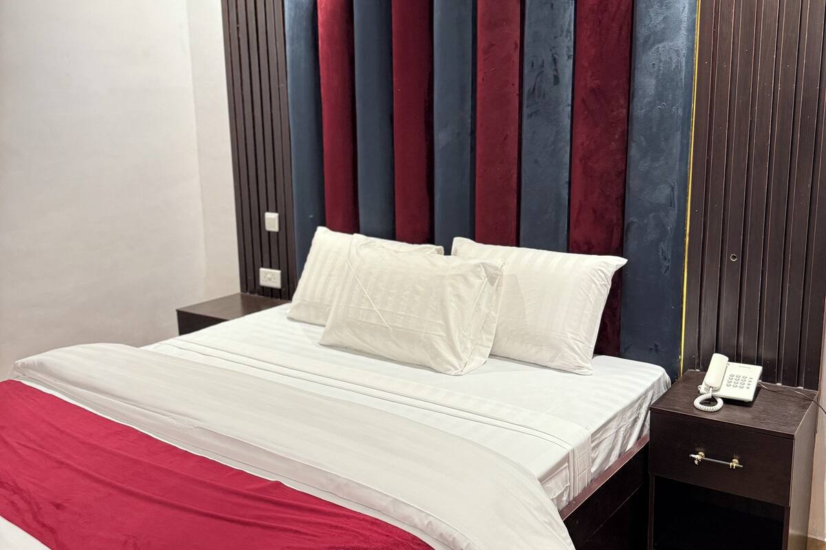 Une chambre moderne avec un lit, du linge de lit blanc, un plaid rouge et blanc, une table de chevet avec un téléphone et un mur avec des lattes de bois verticales.