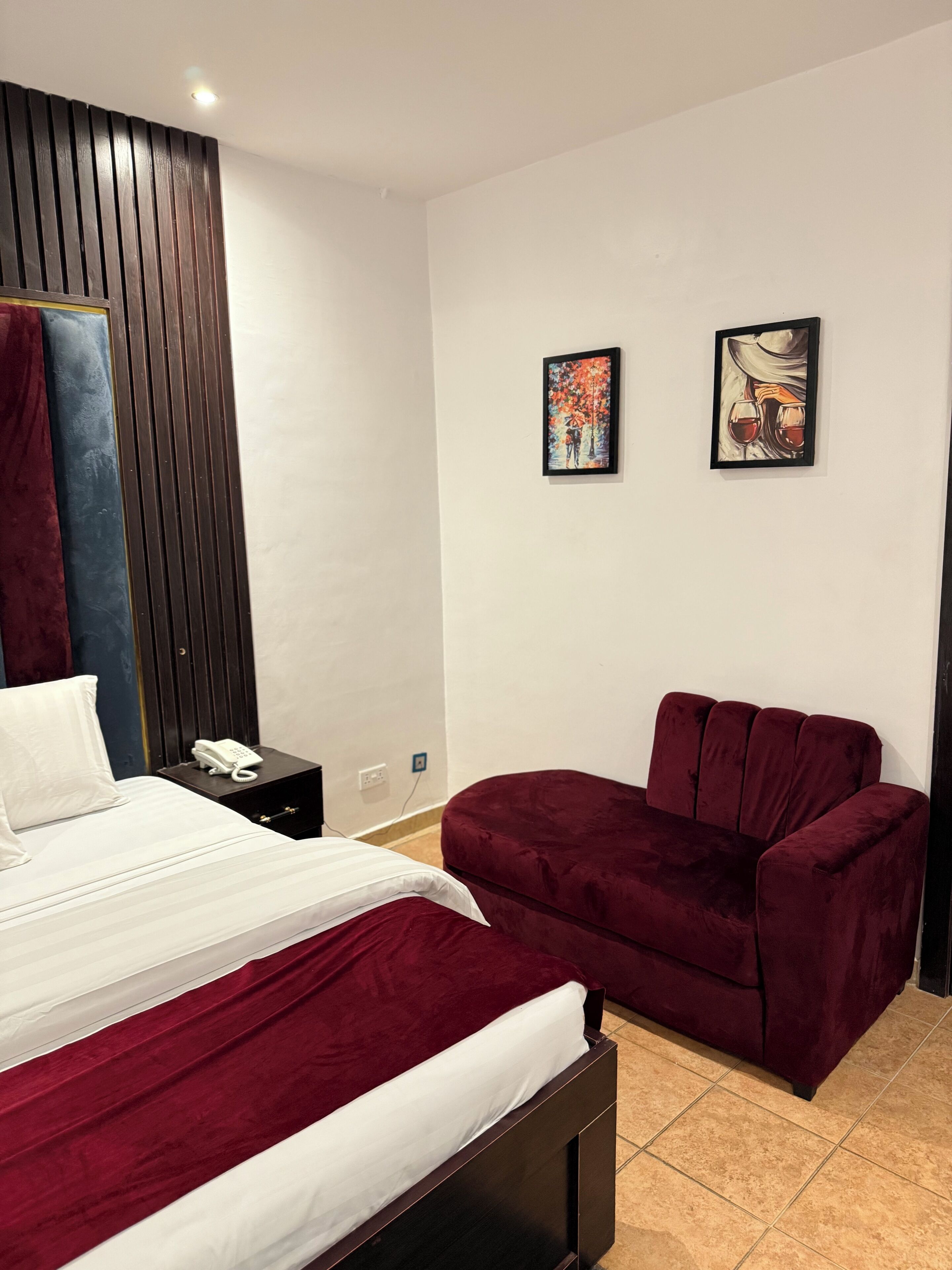 A bedroom with a bed, a nightstand, a chair, and two wall art pieces.