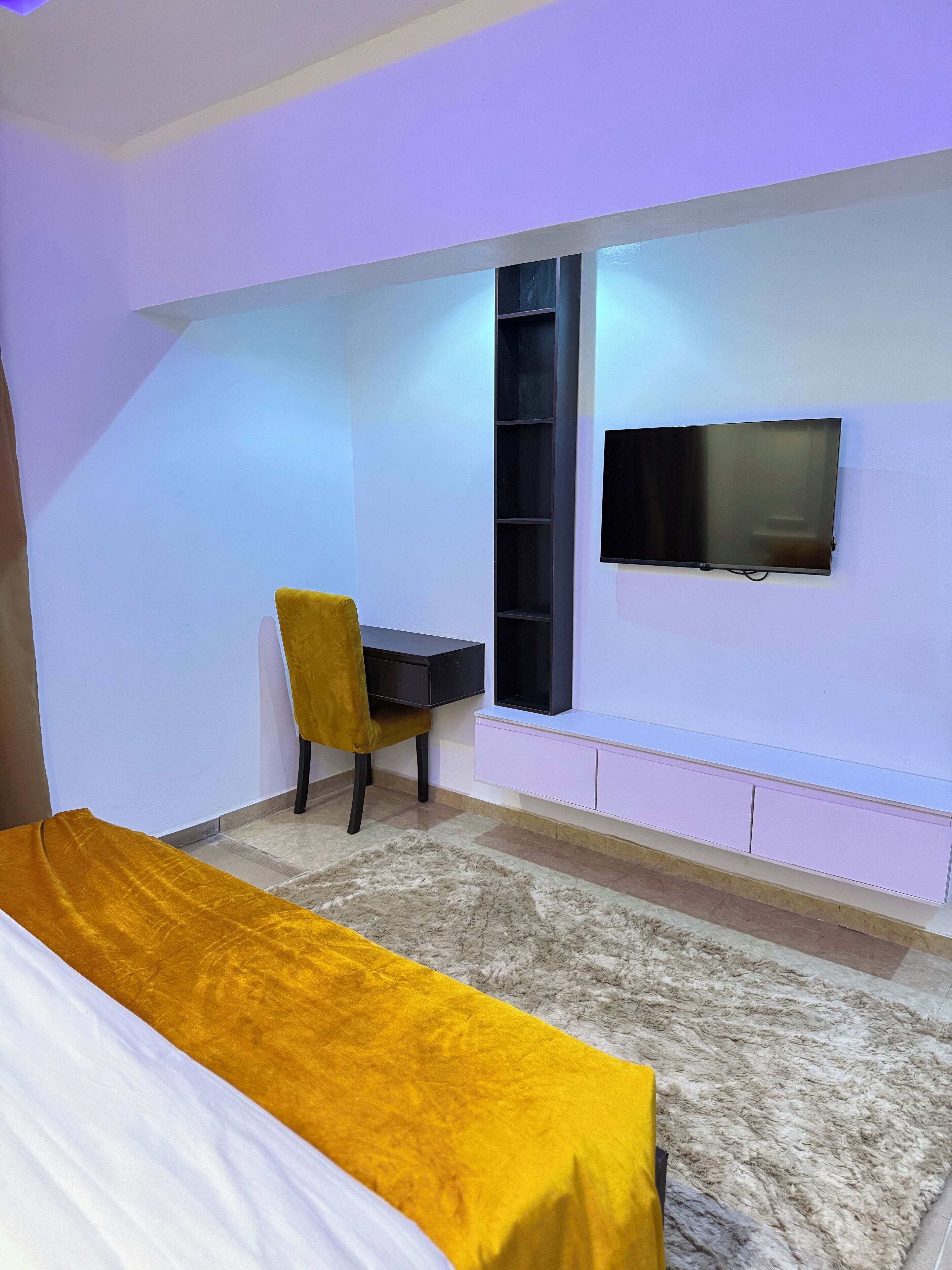 A room with a bed, a desk, a chair, a TV, and a shelf.