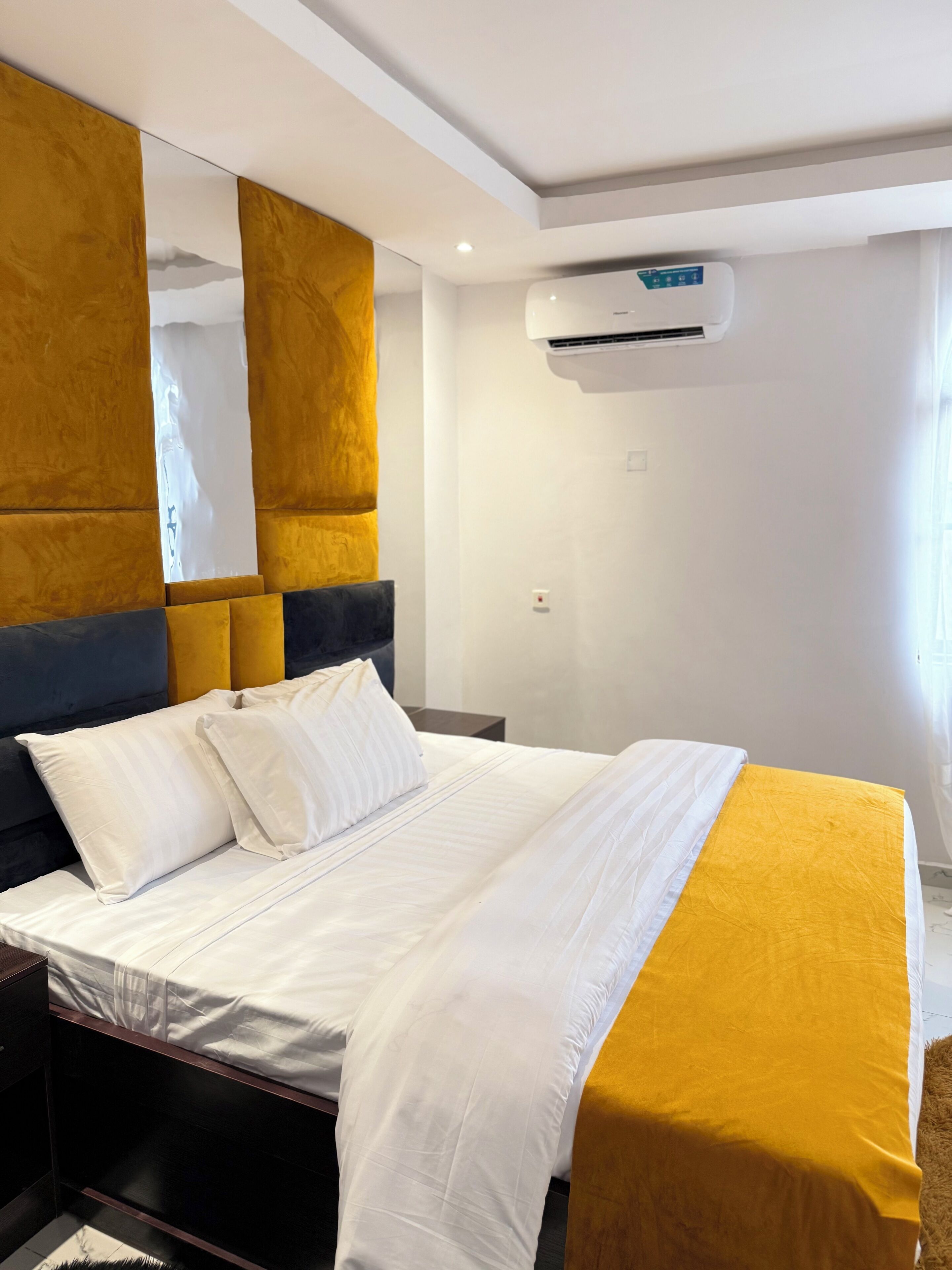 A hotel room with a bed, a large mirror, and an air conditioning unit.