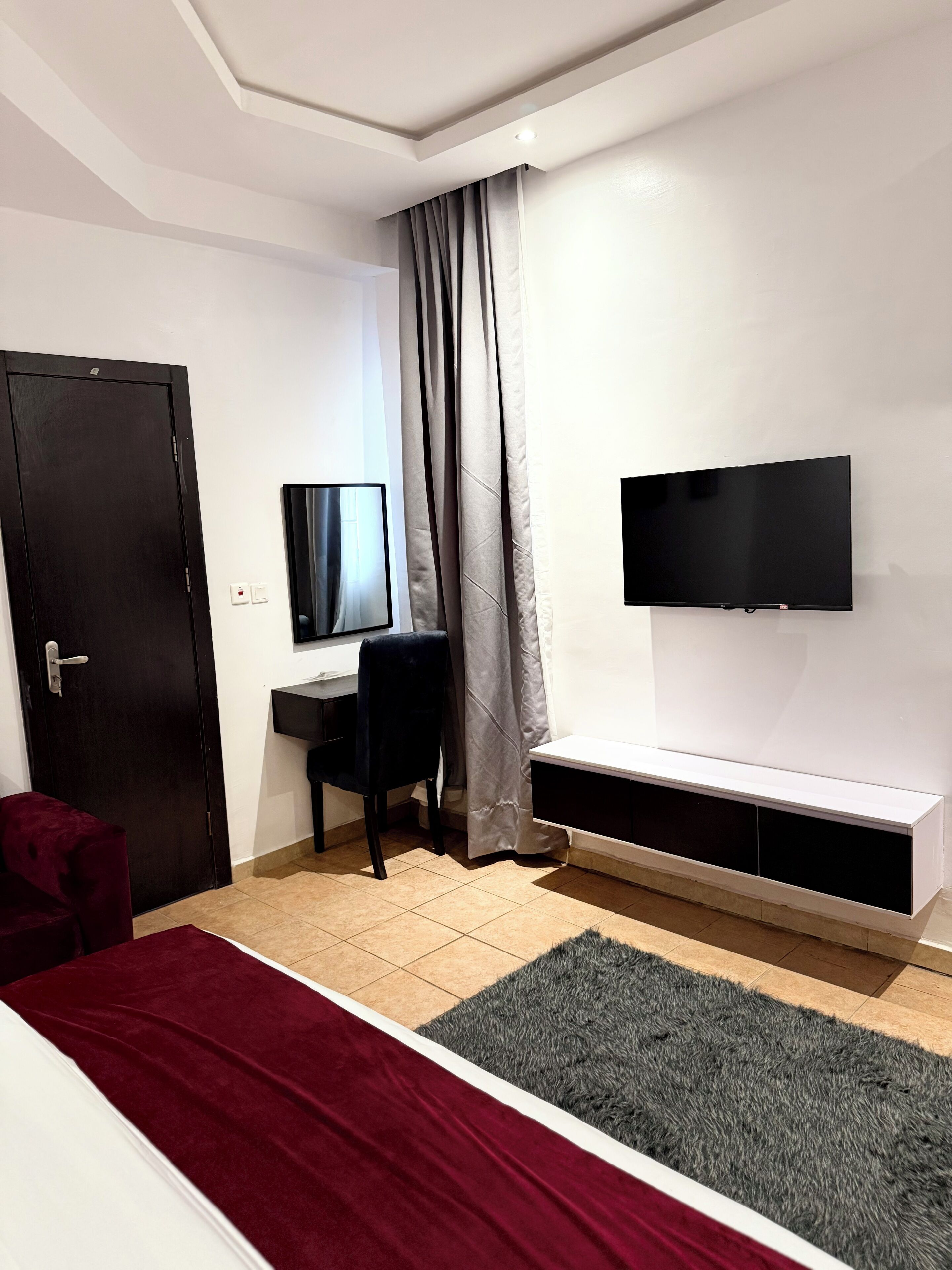 A bedroom with a bed, a desk, a chair, a television, and a window with curtains.