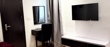 A bedroom with a bed, a desk, a chair, a television, and a window with curtains.