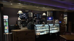 Un restaurante con mostrador de deli, carteles de menú, refrigerador de Pepsi y una máquina de café.