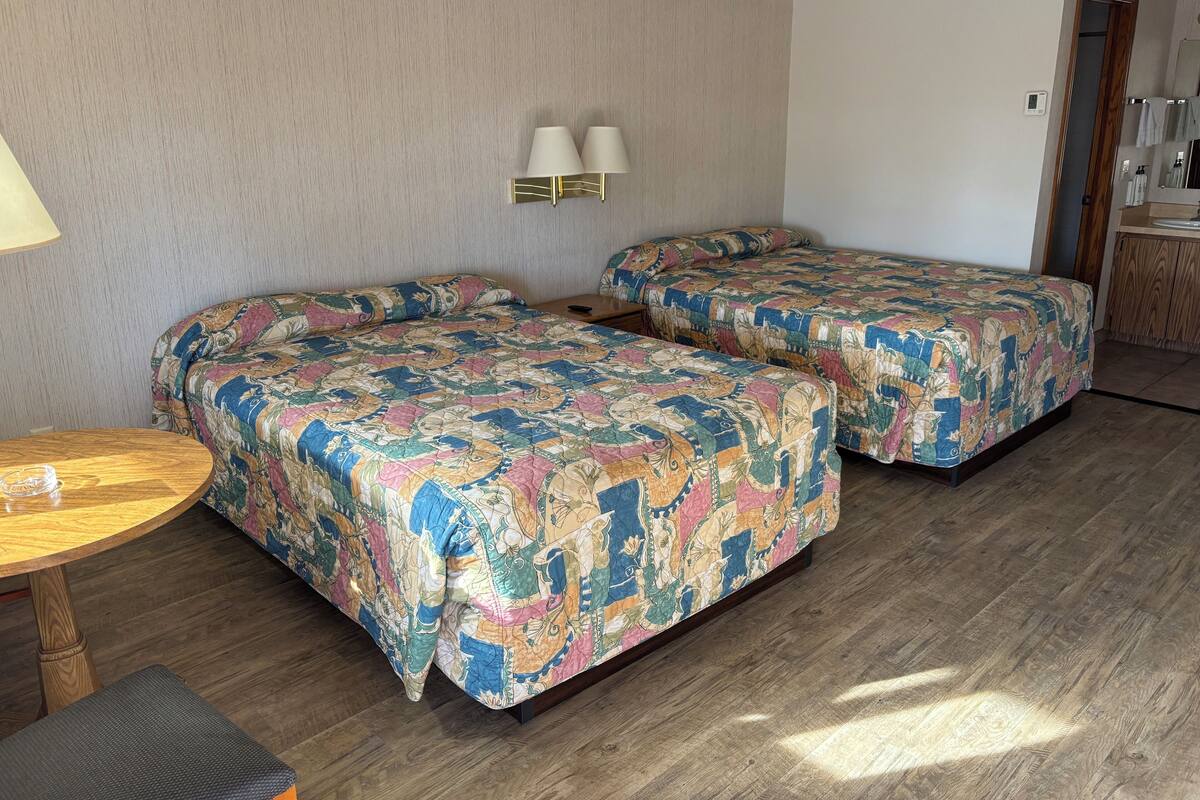 Ett hotellrum med två sängar, ett litet bord och en bänk.