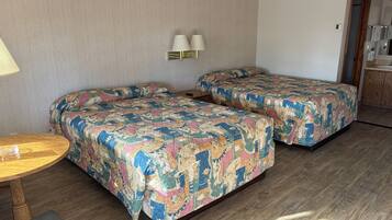 A hotel room with two beds, a small table, and a bench.