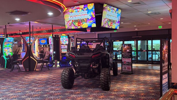 Un salón de juegos interior con varias máquinas recreativas, un cuatriciclo grande y carteles promocionales.
