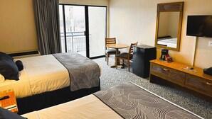 Habitación de hotel con dos camas, un escritorio con silla, cómoda, televisor y un ventanal con vistas al exterior.