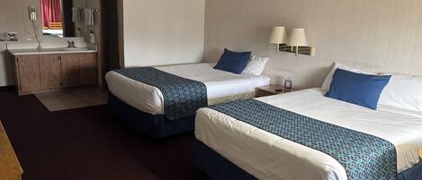 A hotel room with two beds, a desk with a mirror, a vanity with a sink, and a red curtain visible through the doorway.