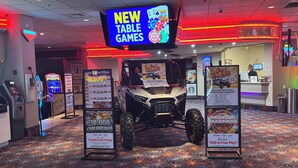 Zona de juegos con un letrero de mesas nuevas, un anuncio promocional de un premio en efectivo de $10,000 y un vehículo Jeep.