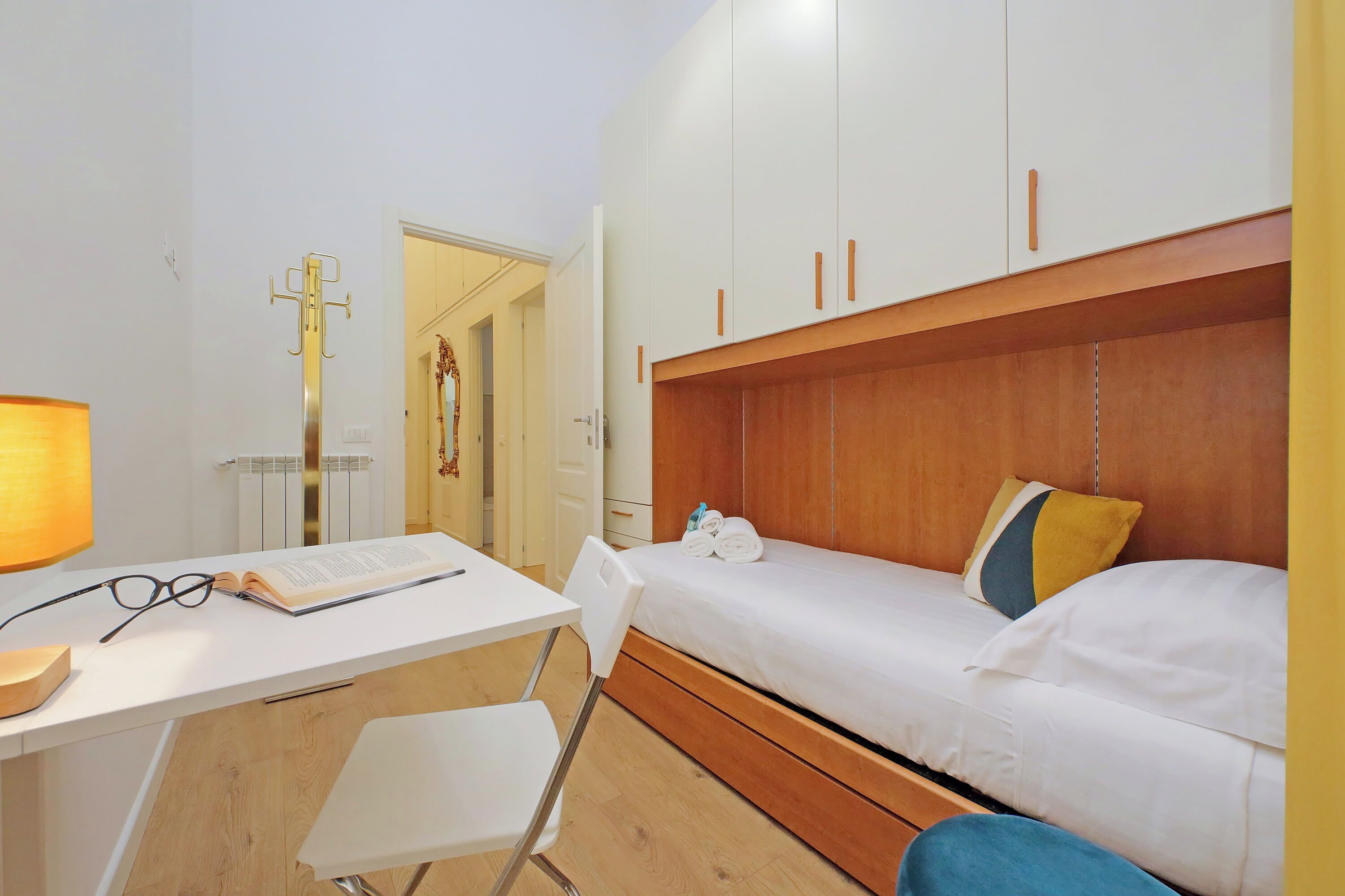 A room with a bed, a desk with a chair, a lamp, and a radiator.