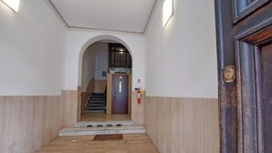 Un pasillo con suelo de madera, una puerta con manija de latón y un extintor en la pared.