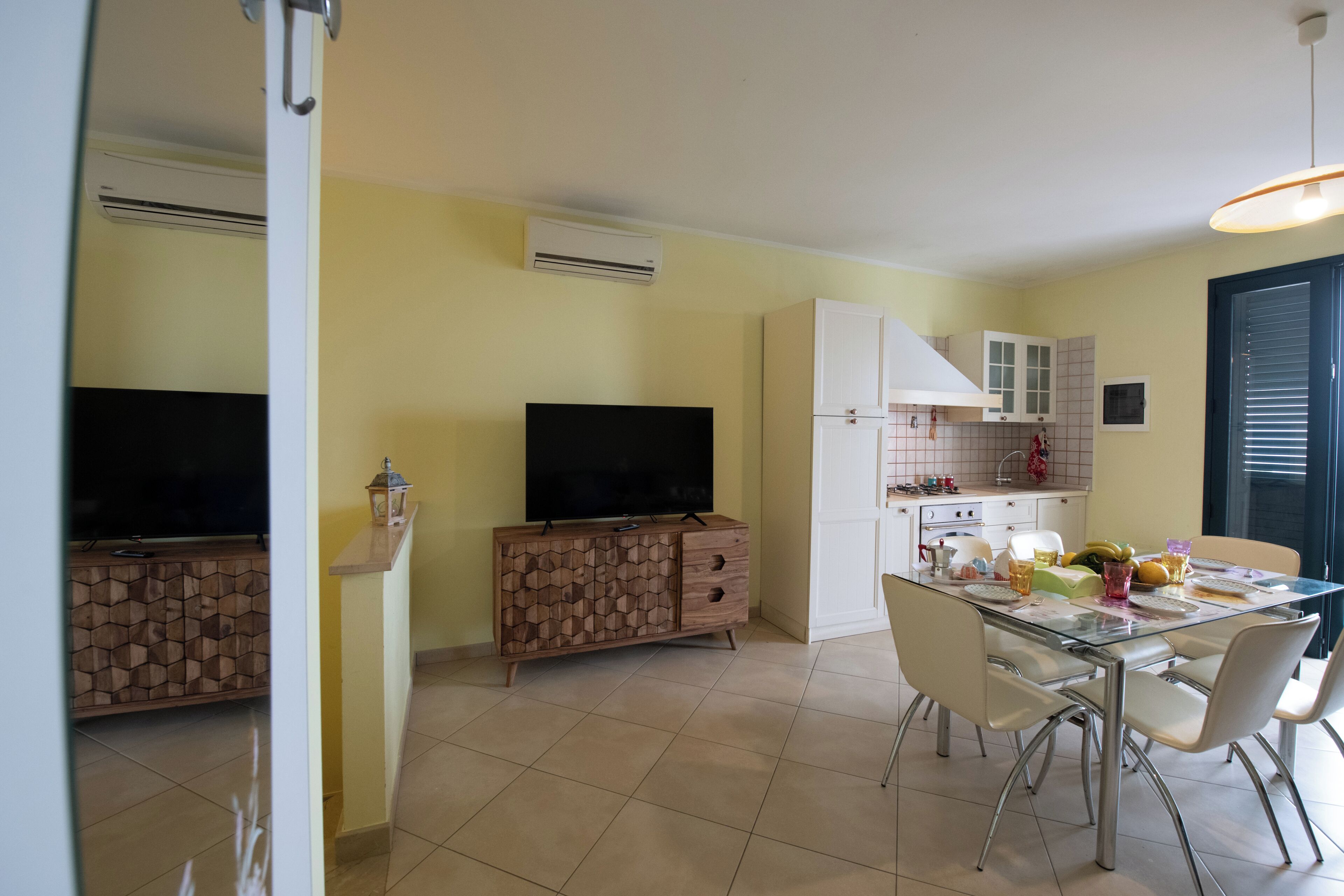Una cocina moderna con armarios blancos, una mesa de comedor con sillas y un televisor de pantalla plana sobre un mueble de madera.