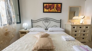 Una cama bien tendida con dos almohadas decorativas, una lámpara de noche, un espejo y un aparador con cajones.