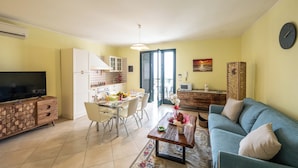 Una sala de estar con sofá, televisión, mesa de comedor y zona de cocina.