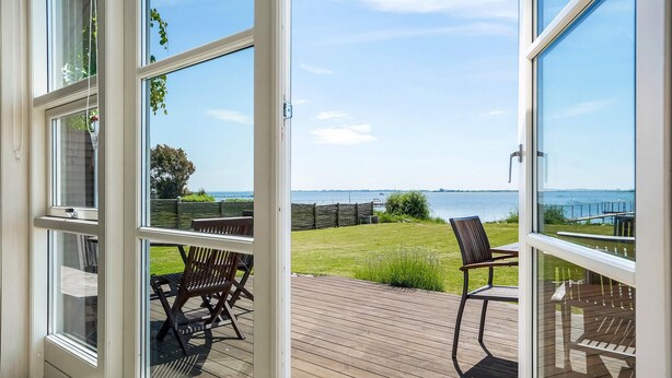 A deck with two wooden chairs and a table, overlooking a grassy area and a body of water. - Gorgeous home in Faaborg with sauna (Faaborg)
