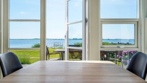 A dining area with a large table and chairs, overlooking a body of water and a grassy area with a dock. - Gorgeous home in Faaborg with sauna (Faaborg)