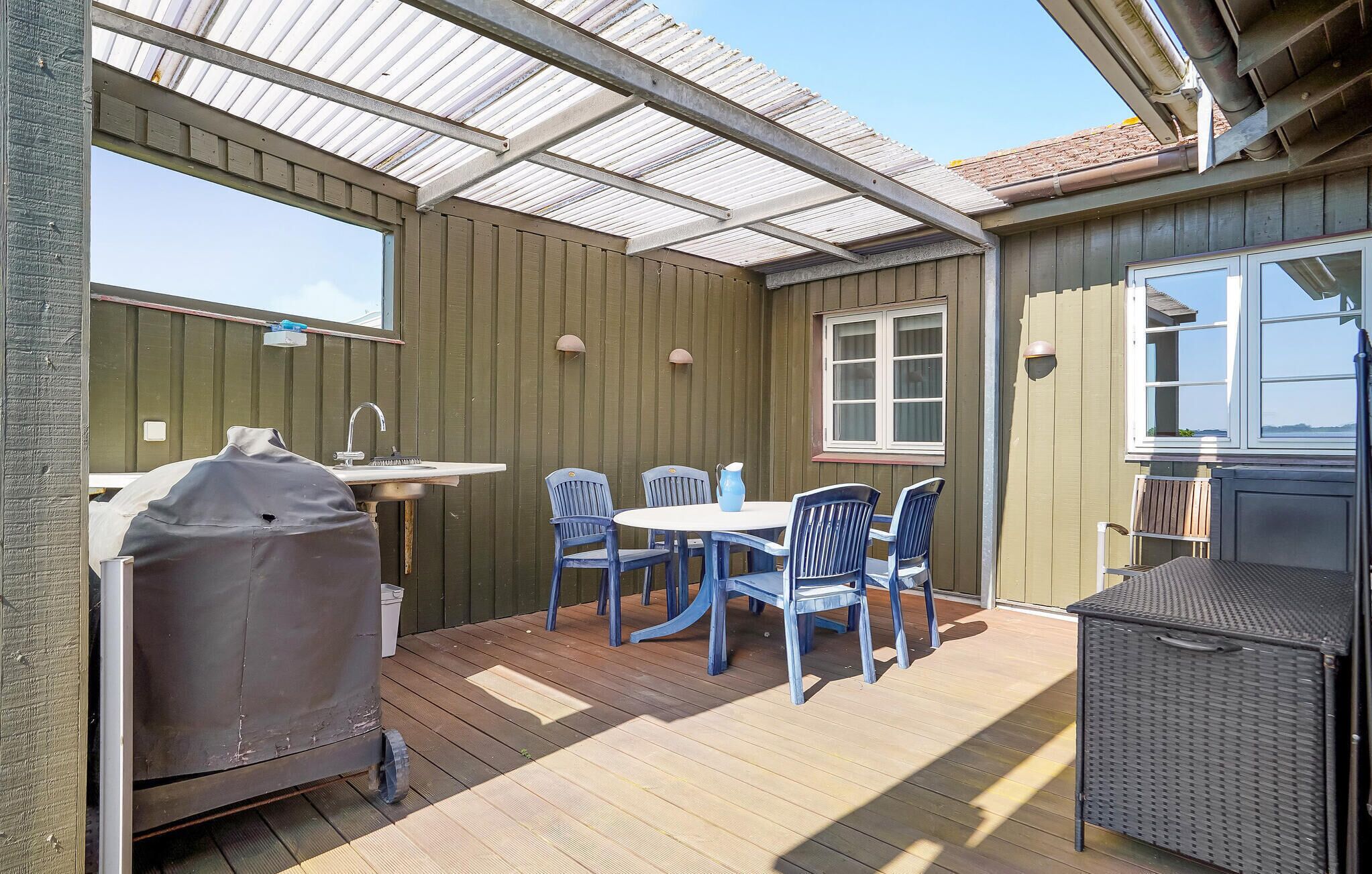 Un patio couvert avec une table et des chaises, un barbecue et une fenêtre.