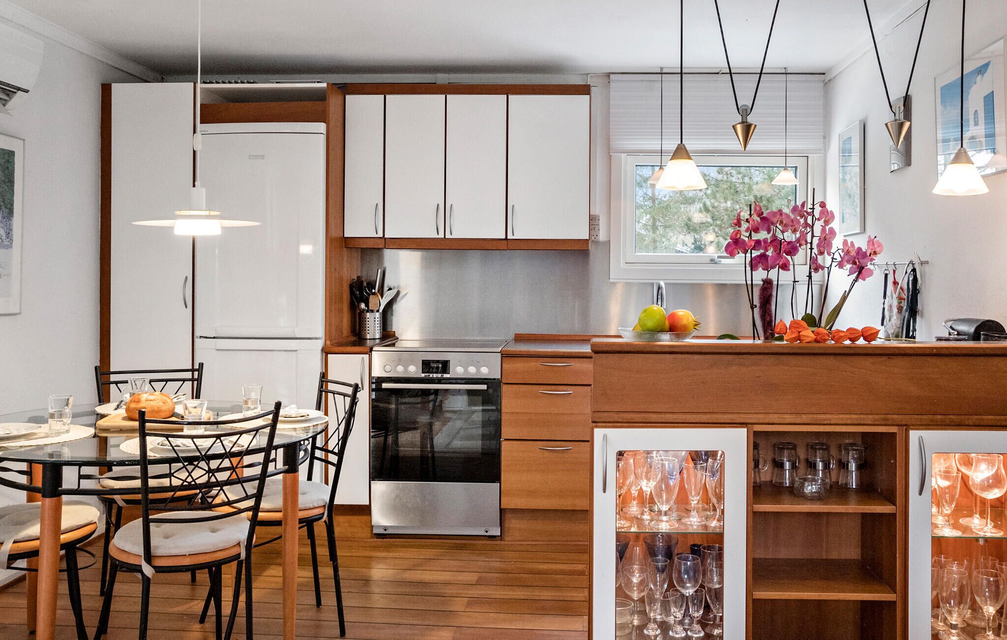 Een moderne keuken met houten kasten, een roestvrijstalen oven, en een eethoek met een ronde tafel en stoelen.