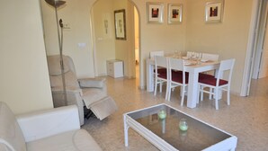 A living room with a white sofa, a glass coffee table, and a dining area with a white table and chairs. - Anacasa Tamarindo Oliva Nova Golf AP1001 (Oliva)