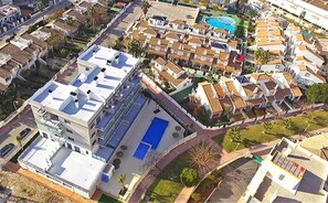 Ein Luftbild eines Wohngebiets mit einem großen Gebäude, das einen Pool auf dem Dach und ein kleineres Gebäude mit einem blauen Schwimmbad zeigt.