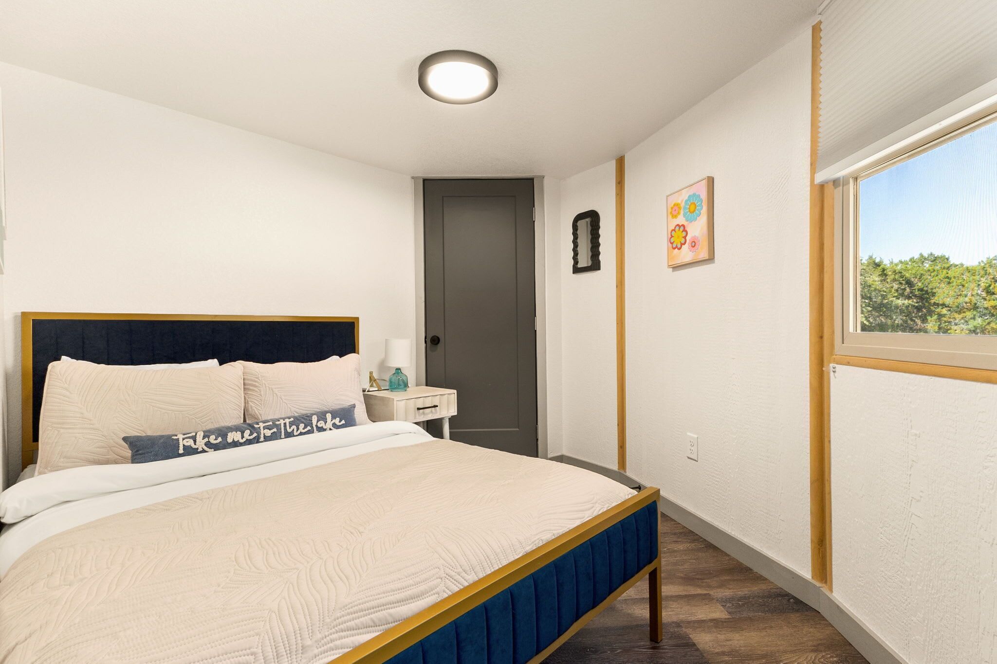 A bedroom with a bed, bedside table, nightstand, and a window with a view.