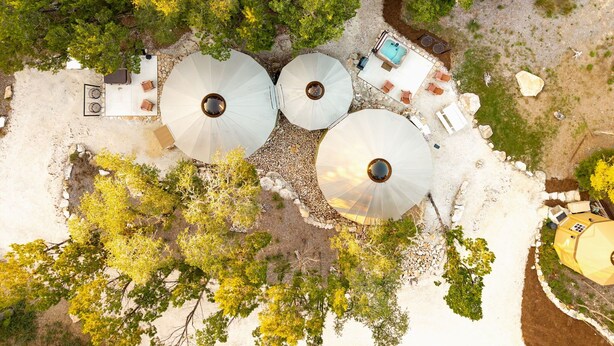 Vista aérea de um resort com três grandes guarda-sóis, área de piscina e vegetação ao redor.