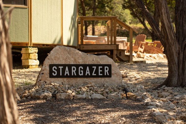 A rock with 'STARGAZER' written on it, surrounded by pebbles and a wooden deck with chairs.
