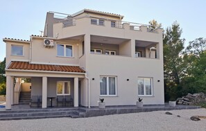 A modern two-story building with a balcony, a covered entrance, and a gravel driveway.