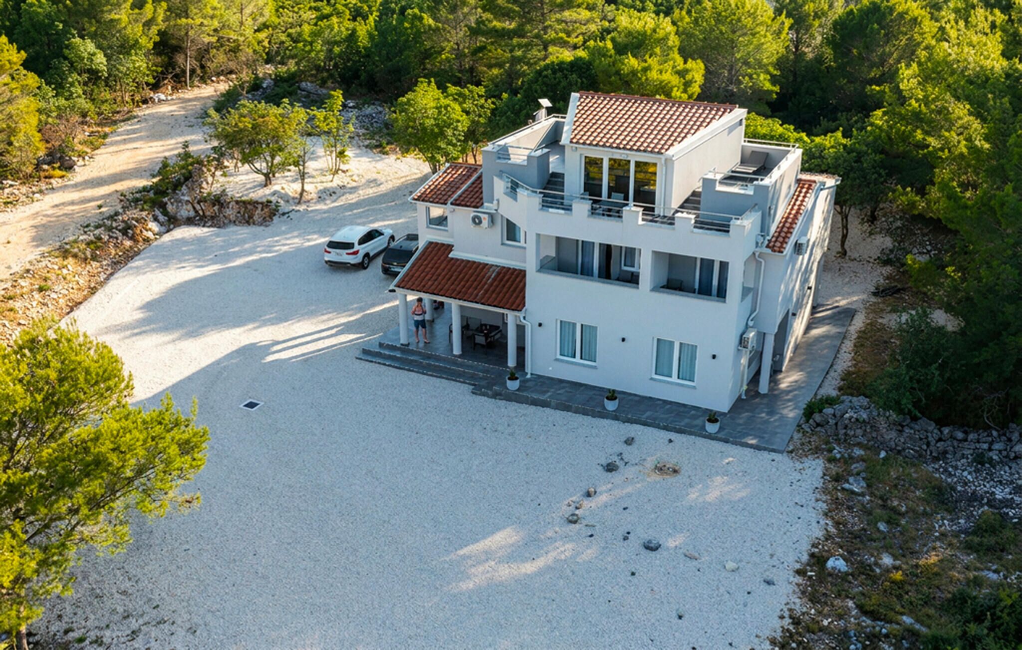 A modern two-story building with a covered patio, a carport, and a gravel driveway.