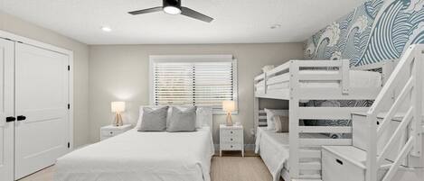 Un dormitorio con una cama, dos mesitas de noche, un ventilador de techo, una ventana con persianas y una litera.