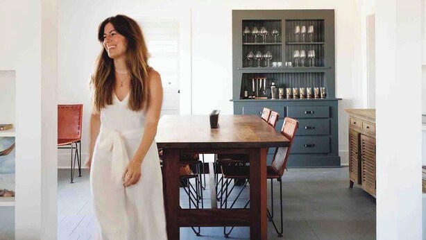 Un comedor con una mesa y sillas de madera, un armario azul oscuro con cristalería, y una puerta blanca al fondo.