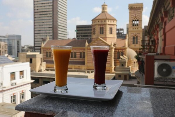 Dos vasos de jugo sobre una bandeja, con un paisaje urbano de fondo.