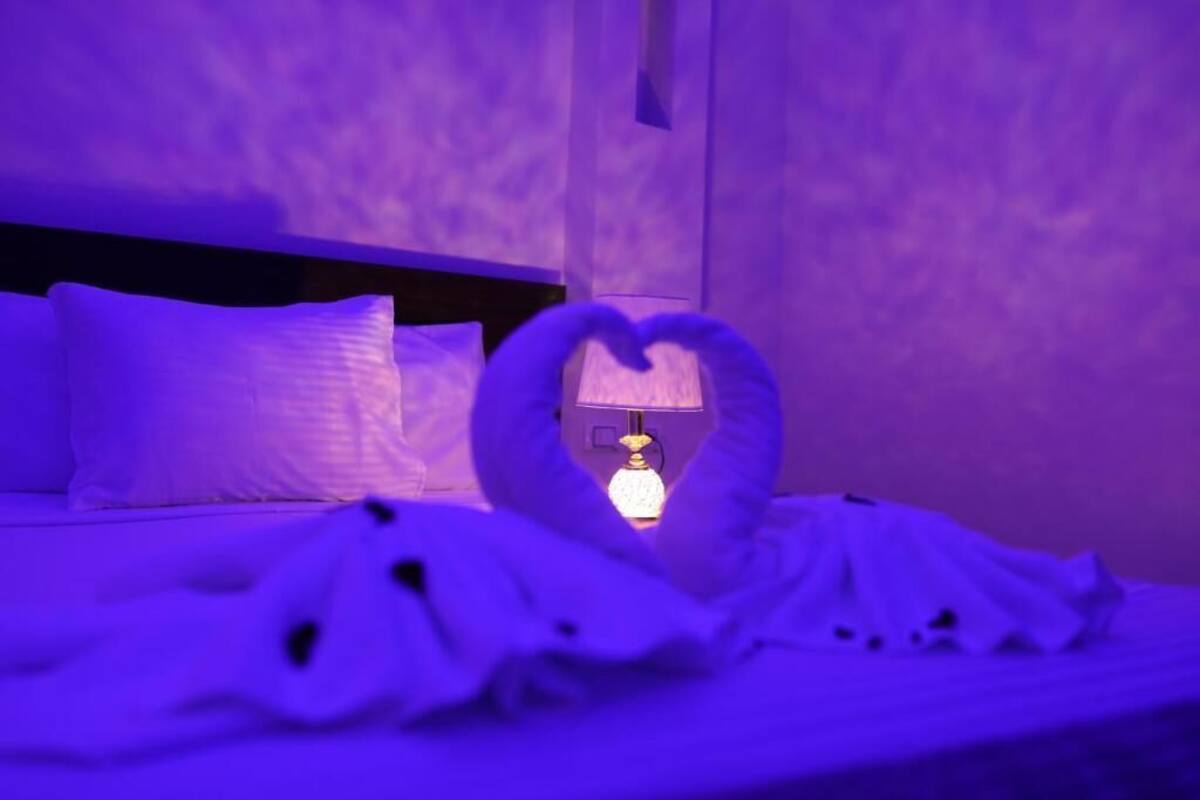 Ein Bett mit weißen Bettwäsche und Kissen, eine Handtuch-Arrangement in Herzform und eine Nachttischlampe.