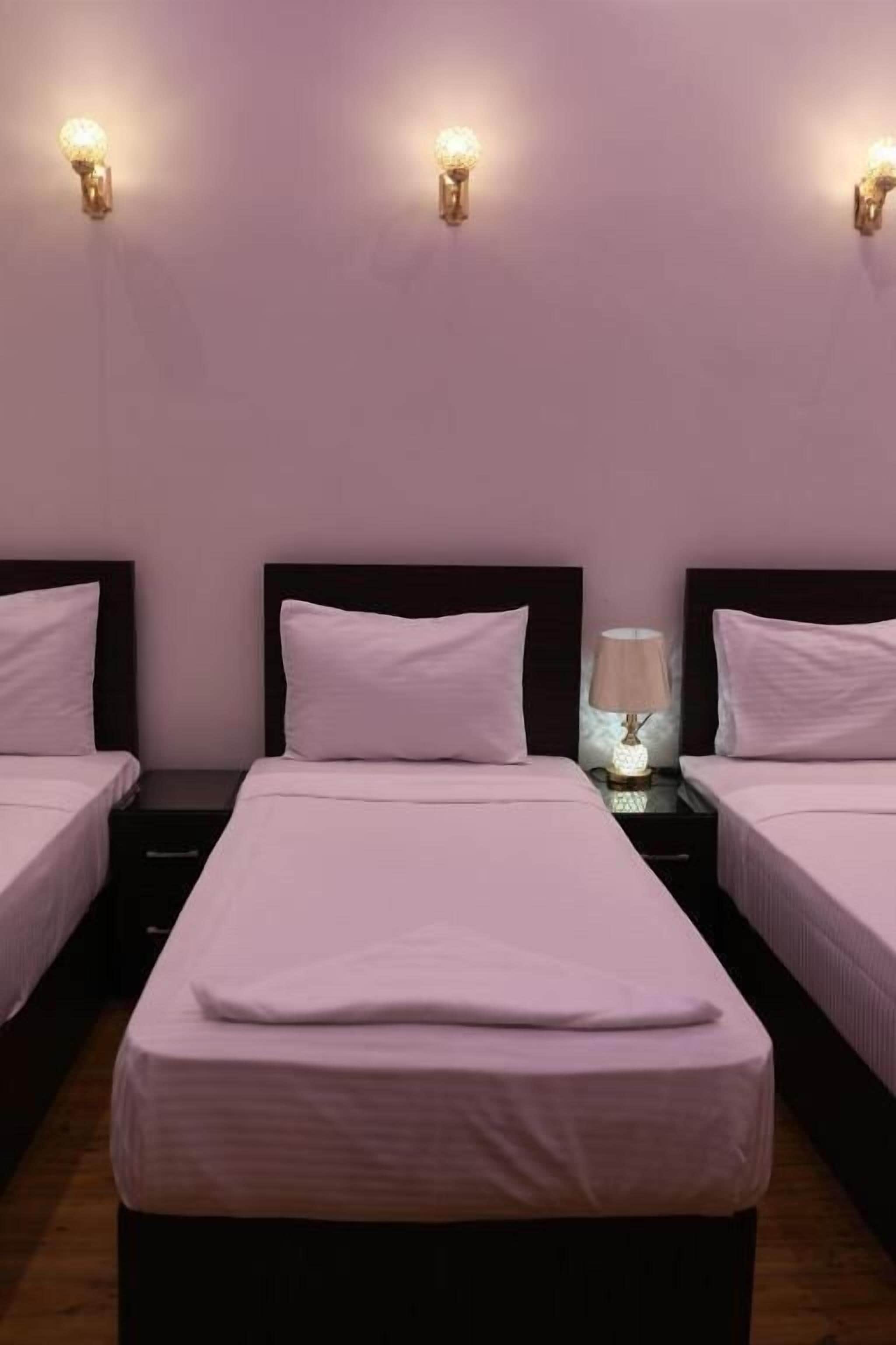A hotel room with two beds, a nightstand with a lamp, and wall sconces.