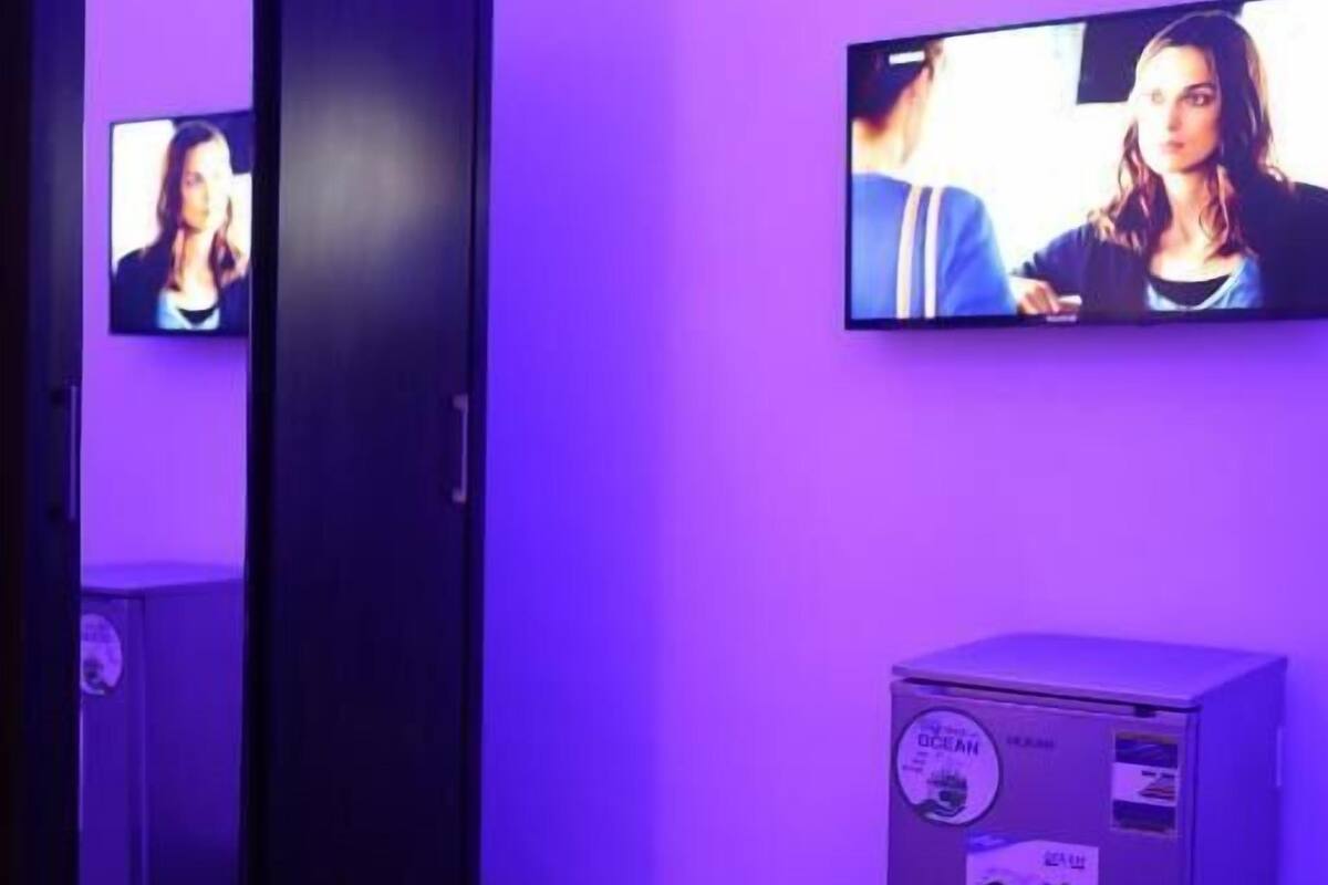 Ein Zimmer mit an der Wand befestigtem Fernseher, einem kleinen Schrank und einer Tür.